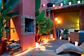 Twilight atmosphere on Mediterranean terrace with lit lanterns and light rope next to house with red lime washed facade