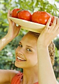 Junge Frau hält einen Teller Tomaten auf dem Kopf
