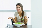 Teen girl eating salad, holding up hand and shrugging shoulders