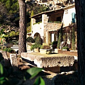 Mediterranean house complex and terrace seating area with weathered stone table top in front of mountain rock face