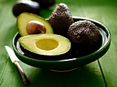 Avocados, whole and halved, in a green bowl