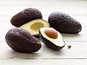 Avocados, whole and halved, on a white painted wooden surface