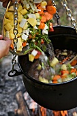 Vegetable soup in a cauldron over a camp fire