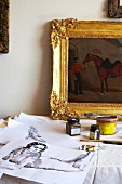 Künsterlatelier: Selbst gemalte Bilder, Malutensilien und Ölgemälde in Goldrahmen auf einem Tisch