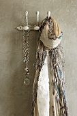 Fringed scarf and necklace hanging from clothes pegs on concrete wall