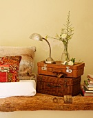 Vase of flowers and retro table lamp on stack of vintage-effect suitcases next to ethnic scatter cushion on floor cushion