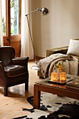 Leather armchair next to vintage standard lamp and simple coffee table on cow-skin rug in corner of lounge