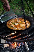 Water being added to a pan of paella being cooked on an open fire