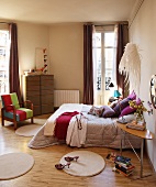 Runde Teppichvorleger vor Doppelbett mit silberfarbenem Plaid und Vintage Stuhl mit farbigem Bezug an Fenstertür