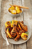 A grill platter with chicken legs, corn cobs and chilli peppers