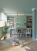 Comfortable floor cushions on animal-skin rug on floor in front of dining table with various chairs in pale blue interior with traditional ambiance