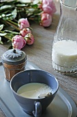Tasse und Glaskaraffe mit Milch, Gewürzdose und Pfingstrosen auf Holztisch