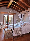 Four-poster bed with metal frame and white bed linen in attic room with rustic wood-beamed ceiling