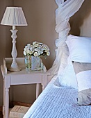 Table lamp and bouquet on rustic bedside table next to bed with scatter cushions