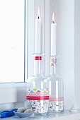 Brennende Kerzen auf Glasflaschen mit Kieselsteinen und bunten Masking Tape Streifen als Badezimmerdeko