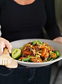 A woman serving beef and chilli salad with carrots