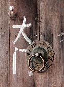 Chinese characters next to metal doorknocker on wooden door