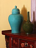 Turquoise china jar with lid next to vase on cabinet painted with floral motifs