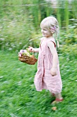 Blondes Mädchen läuft mit Blumenkorb durch den Garten