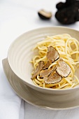 A plate of spaghetti with truffles on a white laid table