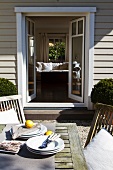 Plates and lemons on terrace table in front of open terrace doors of wooden house with view into interior