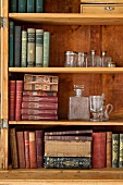 Antiquarian books and glass vessels in open wooden cabinet