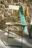 Simple folding chair with scarf and sunhat in front of stone wall