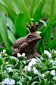 Decorative frog figurine between pulmonaria and allium leaves