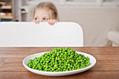 Girl hiding from peas at table