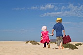 Zwei Kinder gehen mit Koffer am Sandstrand