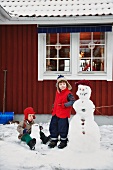 Zwei kleine Jungen bauen Schneemänner vor dem Haus