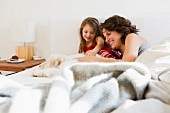 Mother and daughter lying in bed with dog