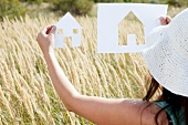 Woman holding up cut-out silhouette of house against meadow
