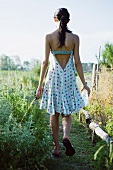 Young woman walking through garden with bottle of water, rear view