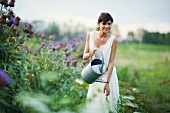 Young woman watering plants in garden with watering can, smiling at camera