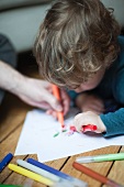 Toddler boy and parent drawing together on paper