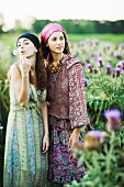 Young hippie women standing in field, one blowing dandelion seeds