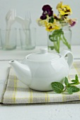 A white teapot with cutlery and pansies in the background