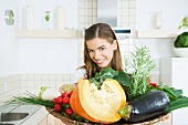 Woman holding tray of fresh vegetables, smiling at camera