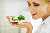 Woman holding up cracker with cucumber slices, smiling