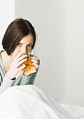 Young woman sitting under covers, drinking hot tea