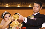 Bride and groom pouring champagne into stacked champagne glasses together