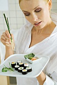 Frau hält einen Teller Maki-Sushi und Essstäbchen