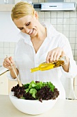 Woman in kitchen, pouring olive oil on large salad