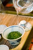 Hot water poured from glass teapot over tea leaves in gaiwan cup