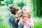 Teen girl helping little sister eat apple