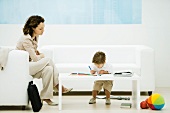 Young professional woman with briefcase sitting in waiting room while son colors