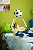 Boy lying on bed idly tossing ball into air