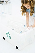 Little girl bending over, placing plastic bottles in recycling bin