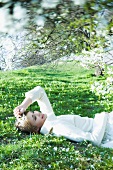 Teenage girl lying on the ground with eyes closed, holding flower, smiling
